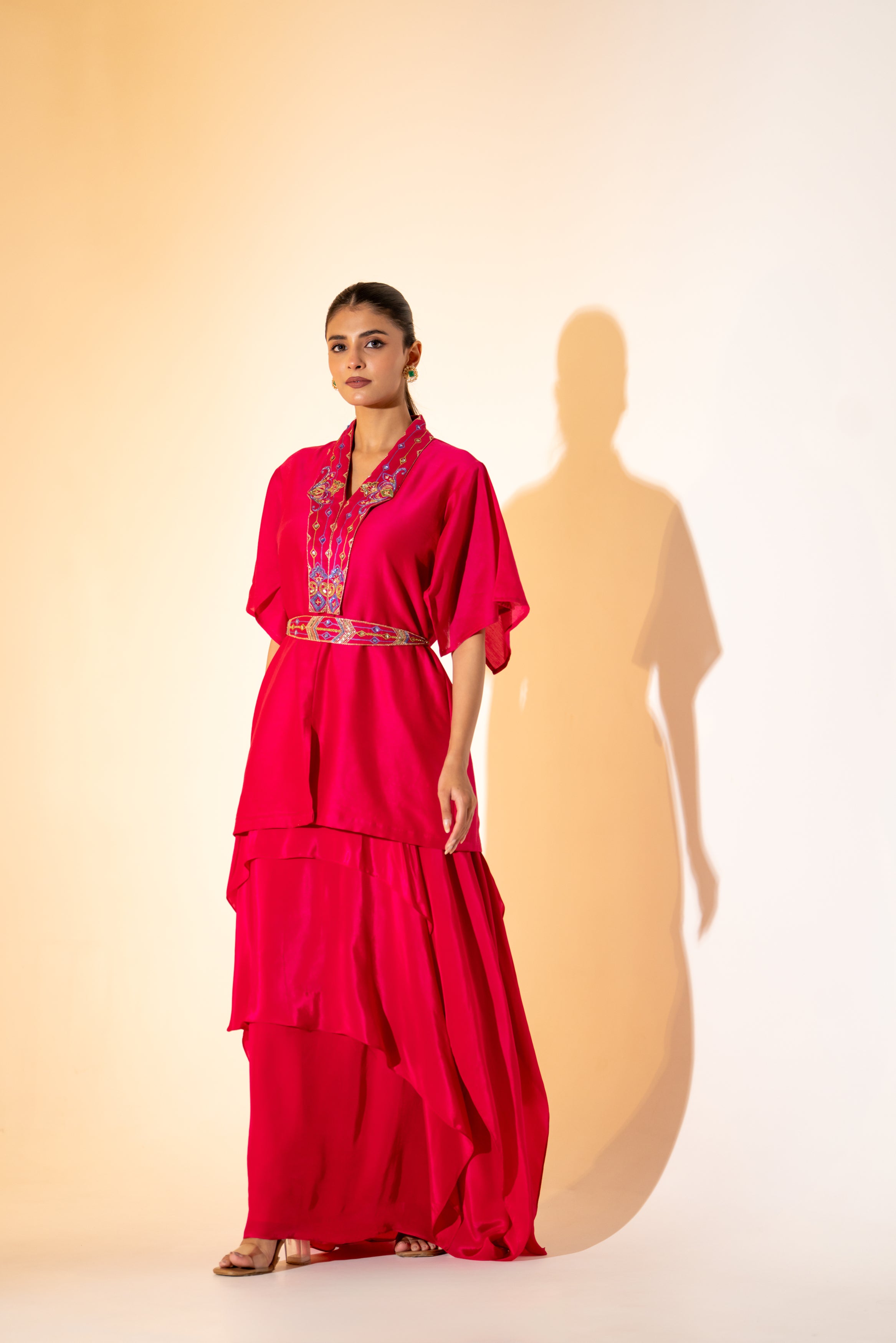 VIBRANT FUCHSIA TOP WITH EMBROIDERED NECKLINE AND BELT PAIRED WITH LAYERED SKIRT.