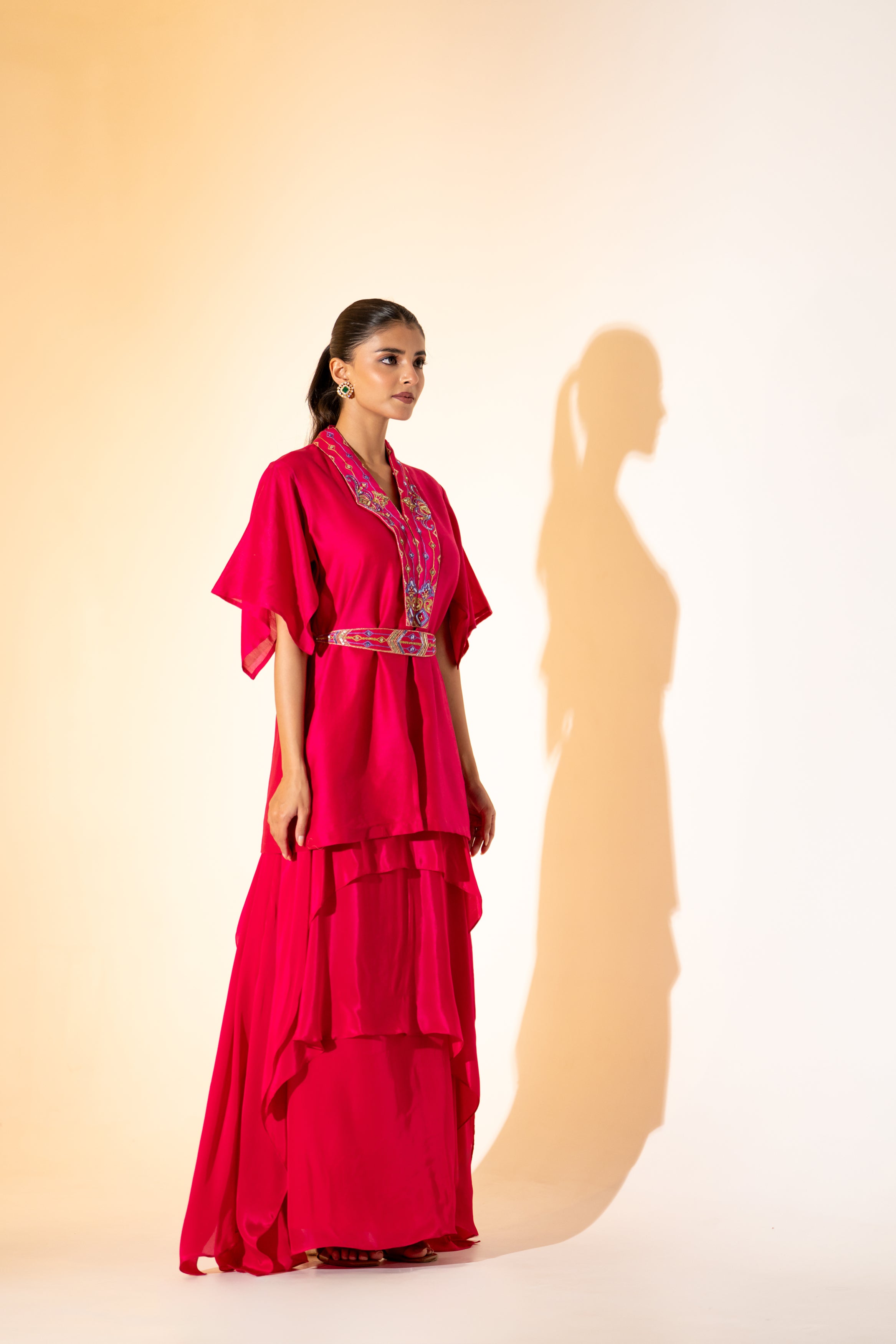 VIBRANT FUCHSIA TOP WITH EMBROIDERED NECKLINE AND BELT PAIRED WITH LAYERED SKIRT.